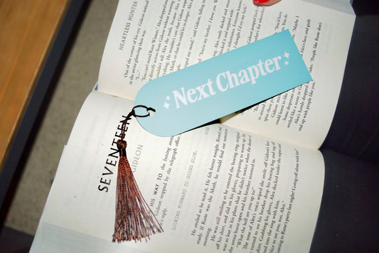 Mint and white Next Chapter Bookmark with brown tassel placed in an open book.