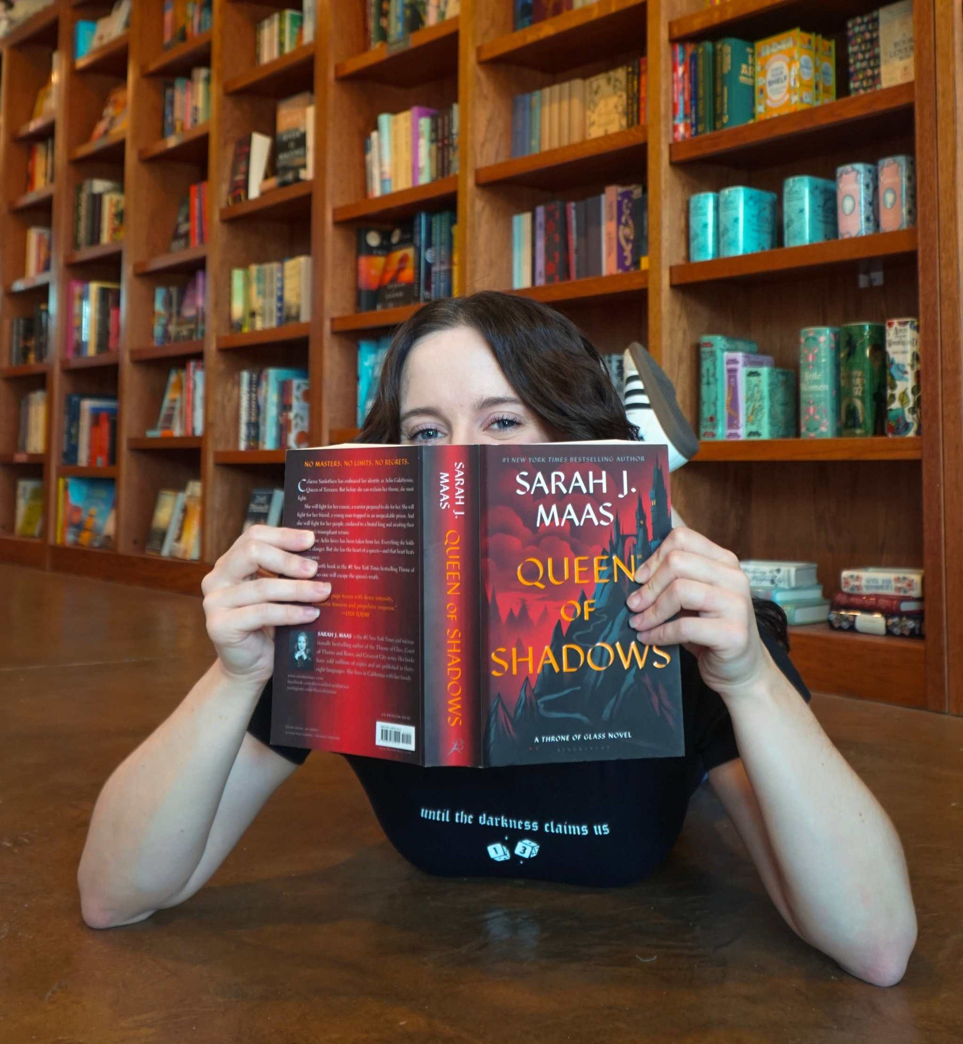 Person holding a book titled 'Queen of Shadows' by Sarah J. Maas in a library setting. The Thirteen Tee from Throne of Glass by Sarah J. Maas. "Until the darkness claims us" Ironteeth Witches design. 