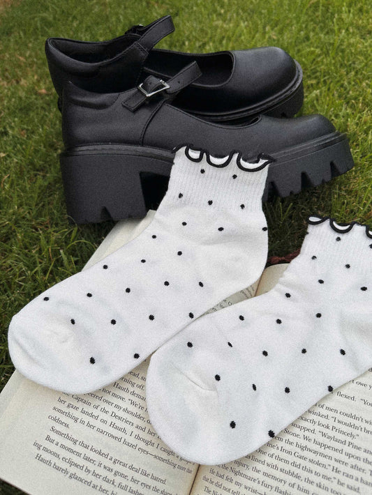 White Gothic Fantasy Reader Socks with black polka dots and ruffle hem paired with black Mary Jane shoes on grass