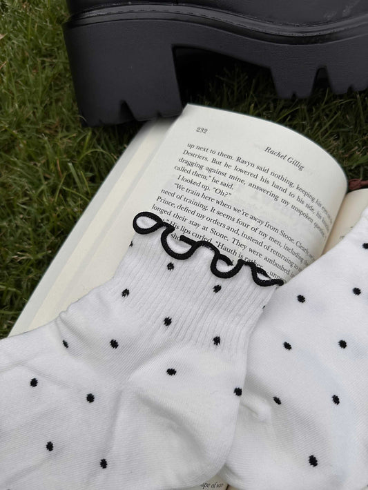 White Gothic Fantasy Reader Socks with black polka dots and black ruffle trim, styled on an open book and black chunky shoe.