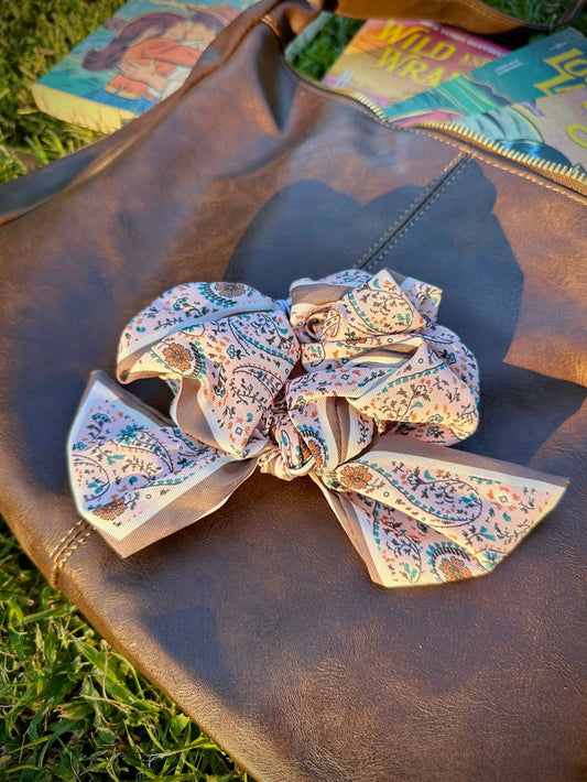 Pink paisley Clementine Scrunchie on brown leather bag outdoors. Inspired by Lyla Sage's cowboy romance book series.