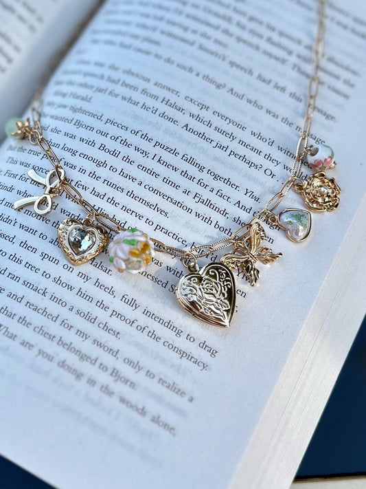 Gold romantasy charm necklace with heart-shaped pendant and other charms on an open book