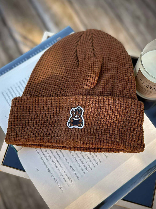 Brown book bear beanie hat with a bookish bear emblem holding a book.