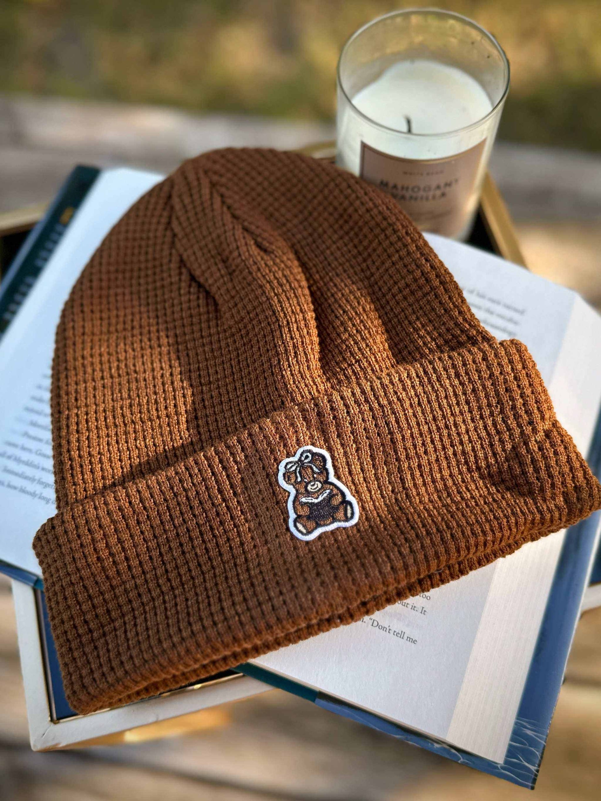 Brown book bear beanie hat with a bookish bear emblem holding a book.