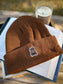Brown book bear beanie hat with a bookish bear emblem holding a book.