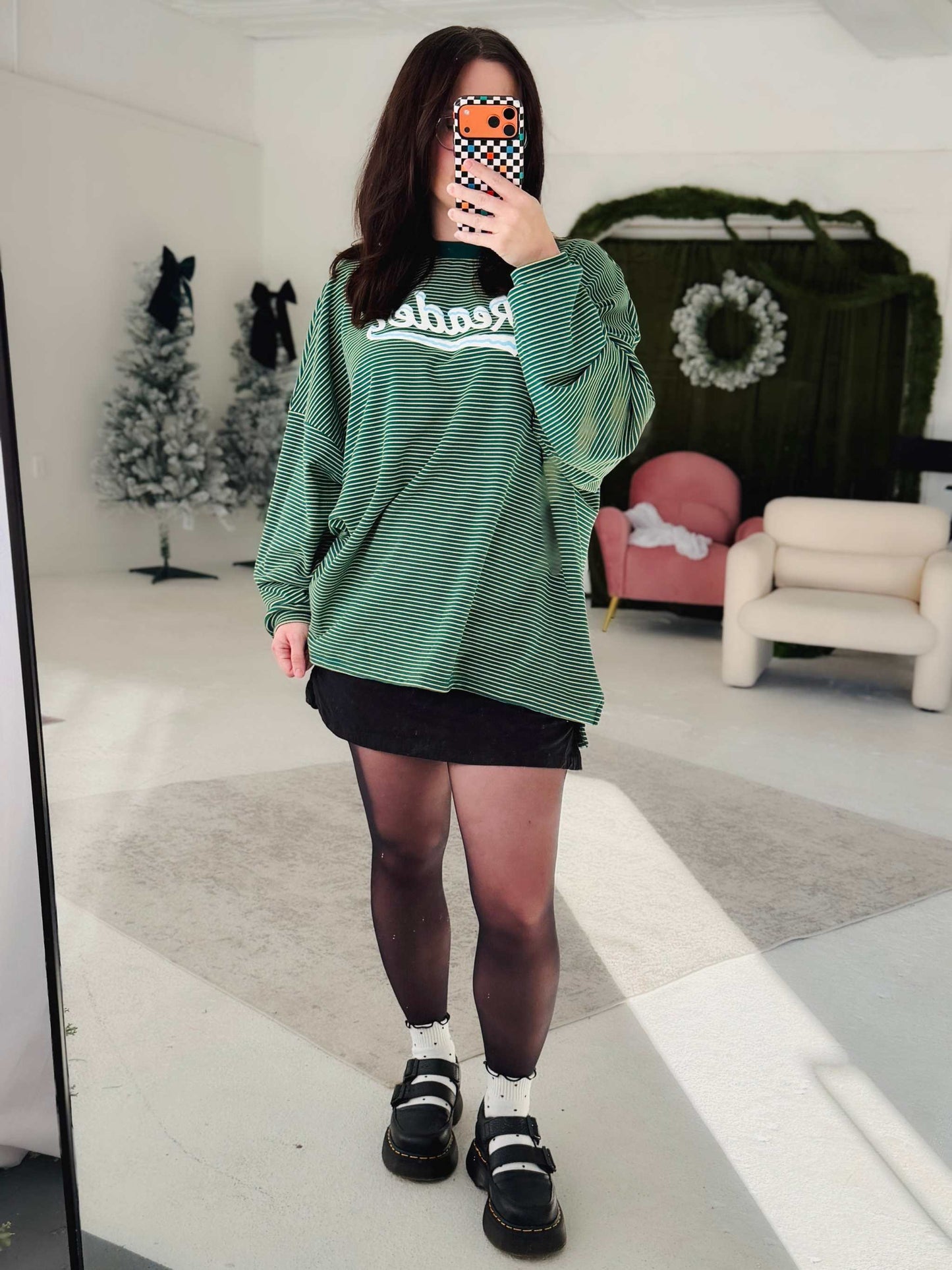 A woman wearing a green Snowy Reader Striped Oversized Top with snowcapped 'Reader' text.