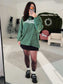 A woman wearing a green Snowy Reader Striped Oversized Top with snowcapped 'Reader' text.