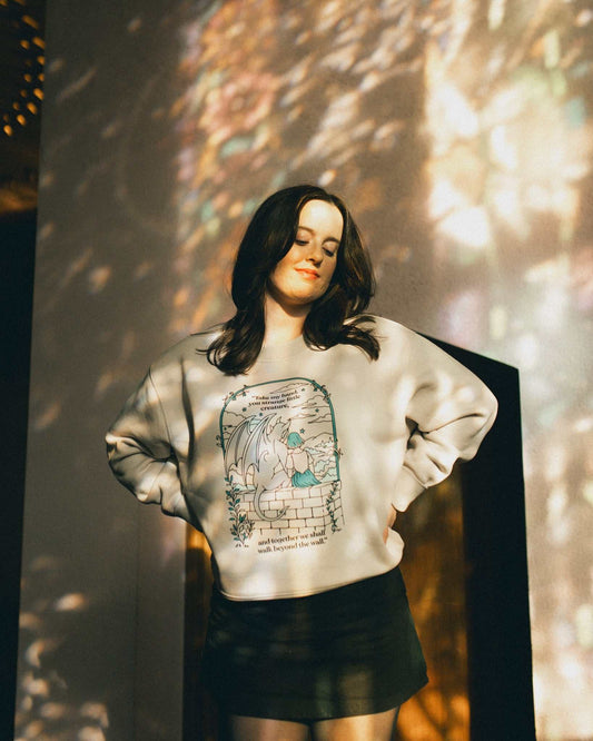 Woman wearing an ivory strange little creatures crewneck sweatshirt with a graphic design inspired by The Knight and the Moth by Rachel Gillig.