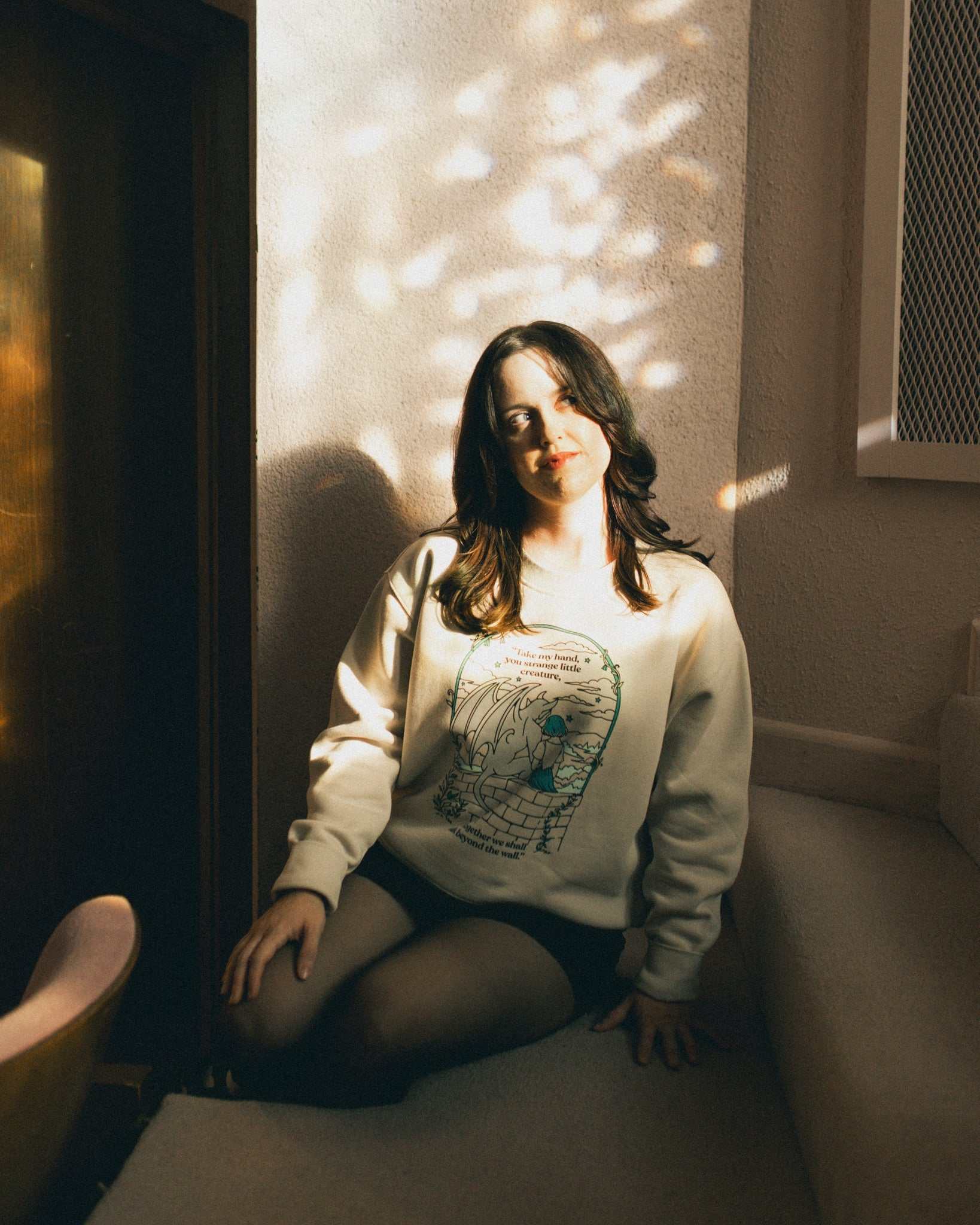 Woman wearing an ivory strange little creatures crewneck sweatshirt with a graphic design inspired by The Knight and the Moth by Rachel Gillig.