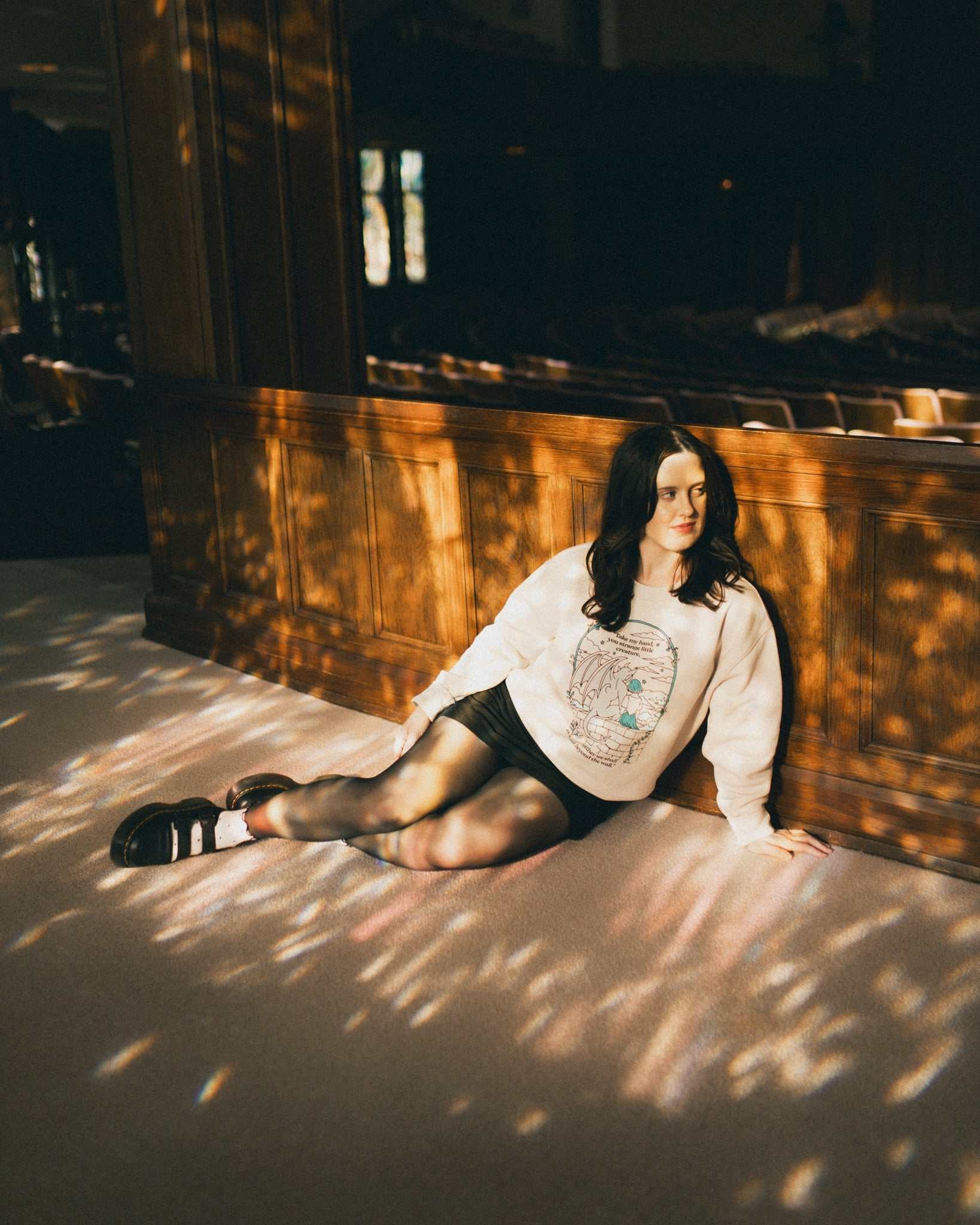 Woman wearing an ivory strange little creatures crewneck sweatshirt with a graphic design inspired by The Knight and the Moth by Rachel Gillig.