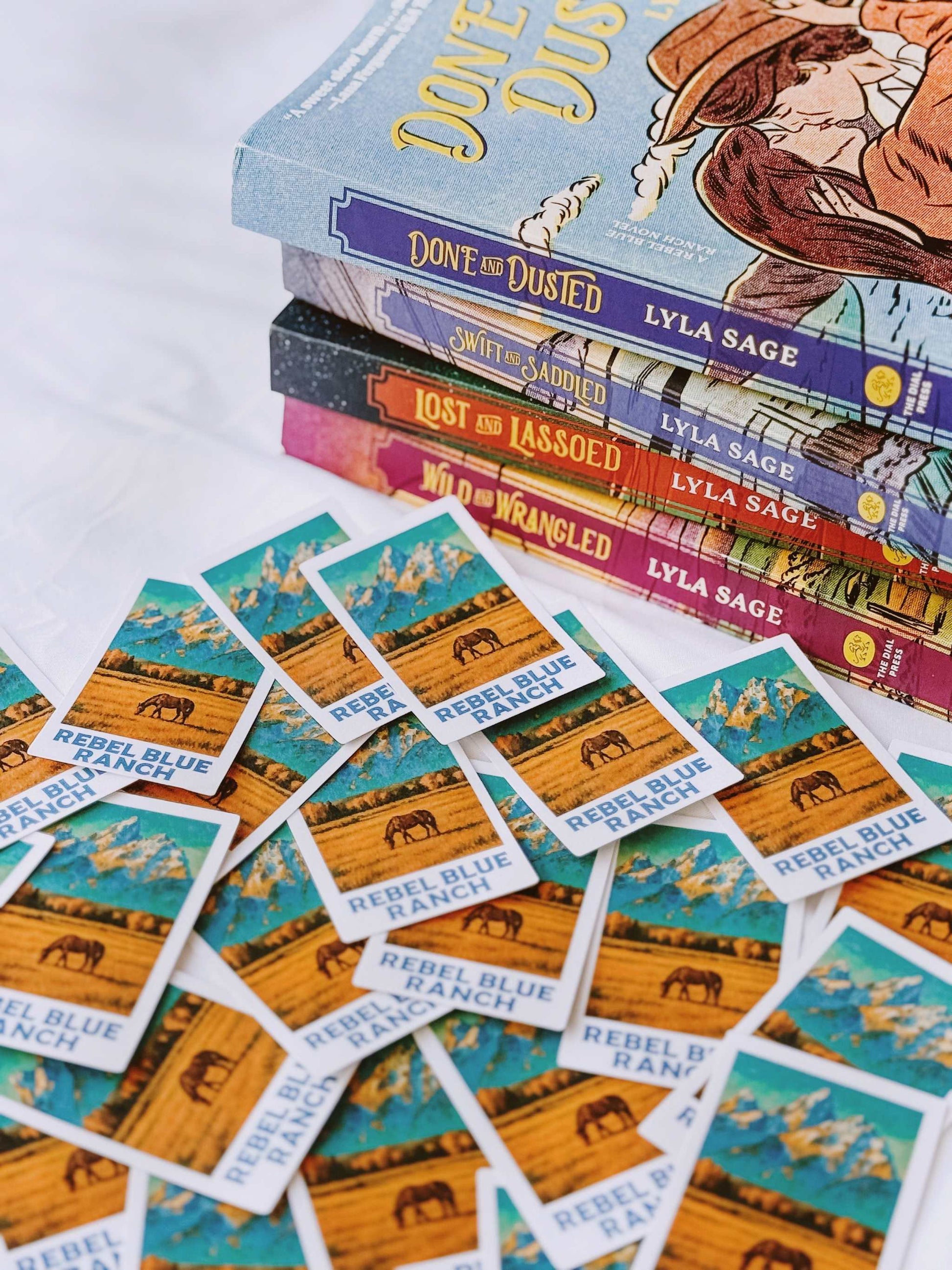 Rebel Blue Ranch Polaroid Stickers from 'Rebel Blue Ranch' by Lyla Sage with a horse and landscape design, placed near other books.