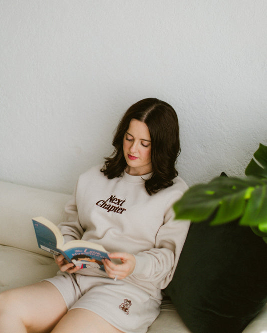 woman reading book wearing ivory Book Bear Shorts with embroidered bear detail and matching Next Chapter Crewneck pullover