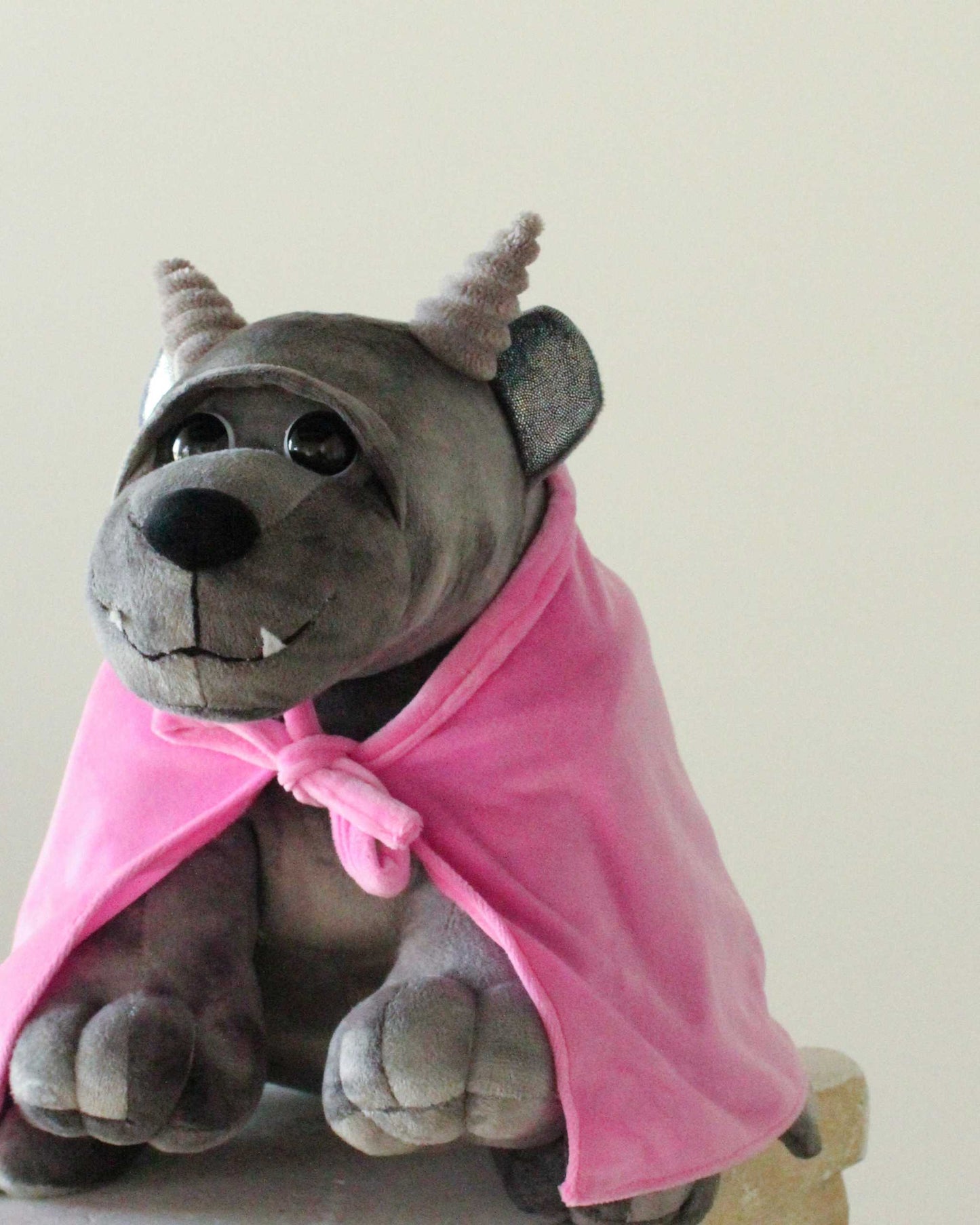 Bartholomew Gargoyle plush in dark gray fabric with textured horns, toothy smile, and a bright pink cloak