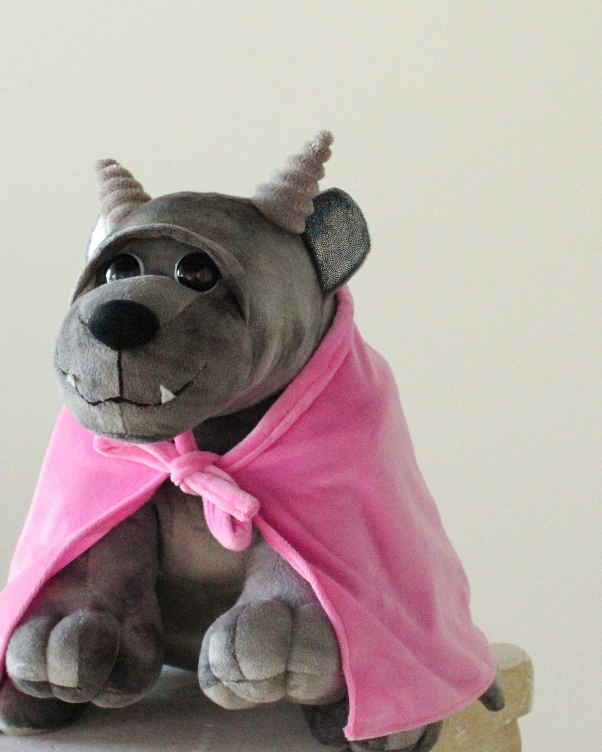 Bartholomew Gargoyle plush in dark gray fabric with textured horns, toothy smile, and a bright pink cloak