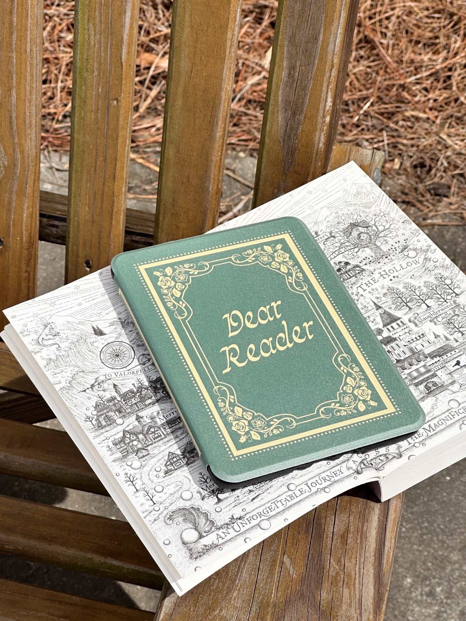 Small green kindle case that looks like a book with 'Dear Reader' on an open book. The Dear Reader Kindle case from Next Chapter is inspired by the Taylor Swift song 'Dear Reader.' The case has a vintage and soft feminine style and looks like a real book.