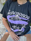 Person wearing a black t-shirt with 'The Ouroboros' design outdoors. A black graphic tee with 'The Ourororos' design featuring an eye, mirror, and purple mist. Inspired by the A Court of Thorns of Roses book series by Sarah J. Maas.