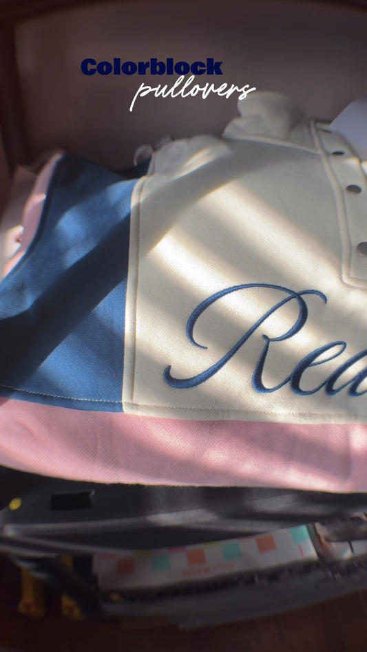 The Reader Colorblock Pullover from Next Chapter is oversized, with a quarter button-up style. It has the word 'Reader' embroidered across the front. Next Chapter offers high quality bookish merch and apparel.