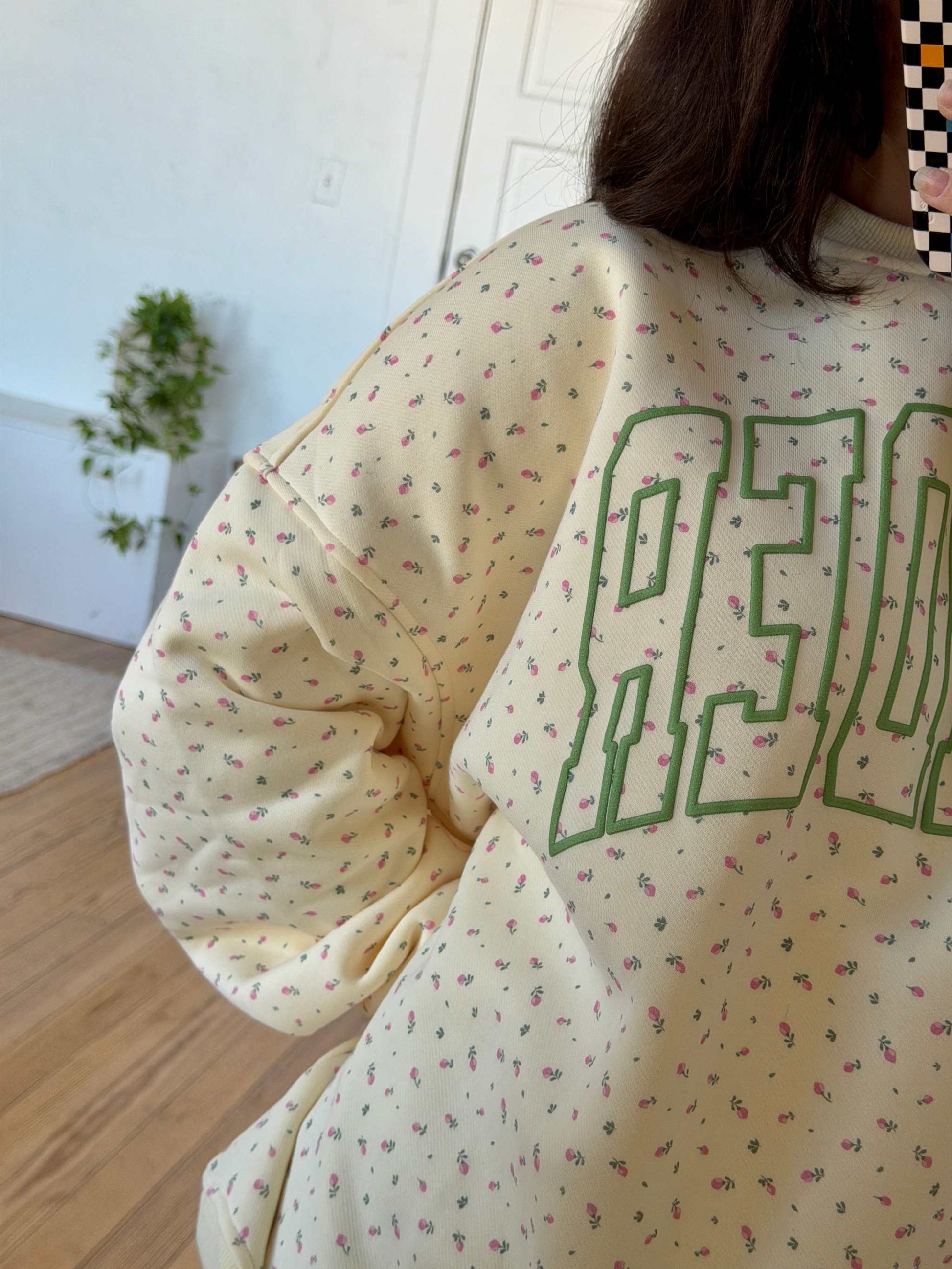 The Reader Floral Crewneck sweatshirt from Next Chapter. Features a floral pattern with green puff print that says 'Reader' across the front. Next Chapter offers high quality book merch and apparel for readers. 