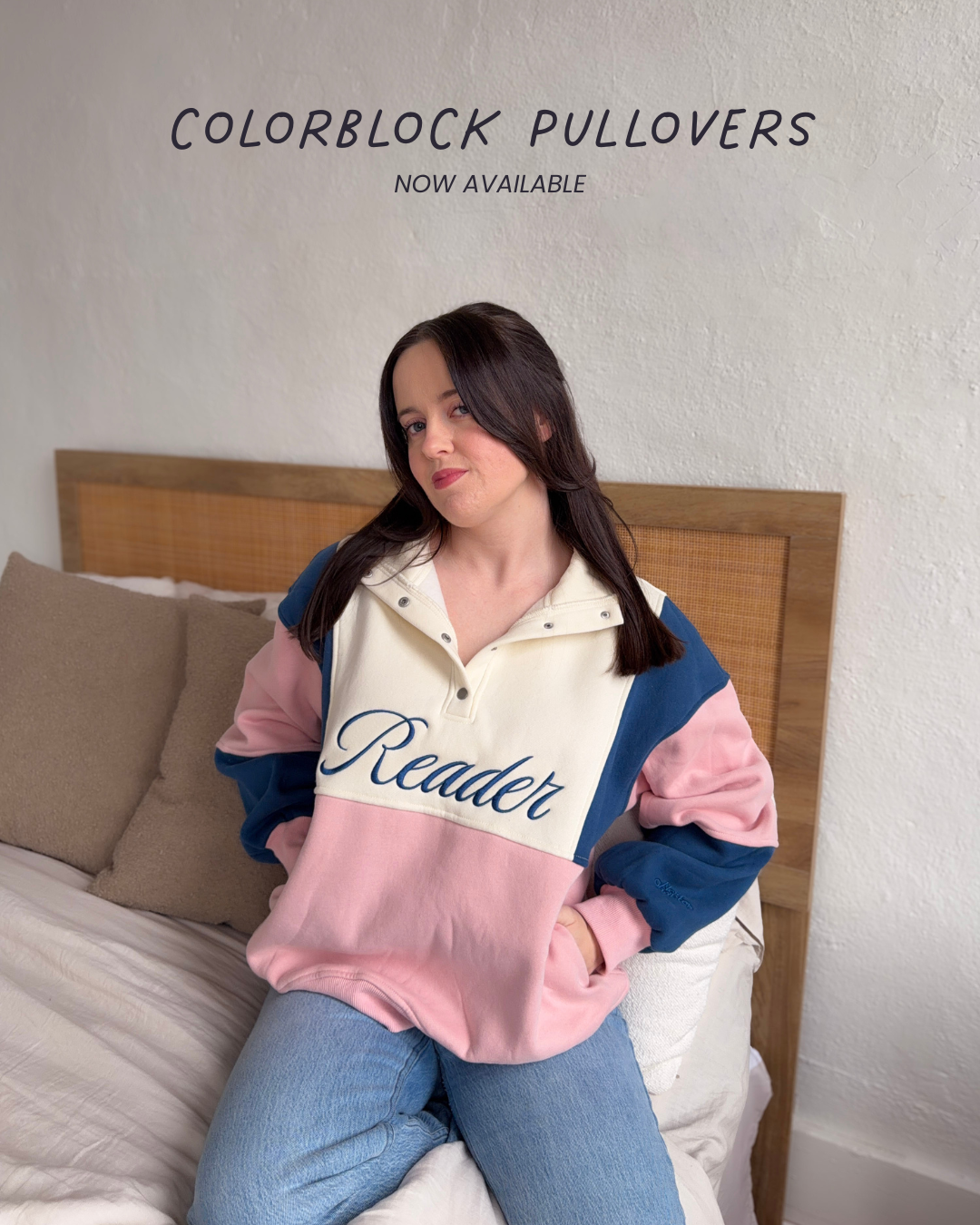 Woman wearing a colorblock pullover with 'Reader' text, sitting on a bed with text on the image that says 'now available'