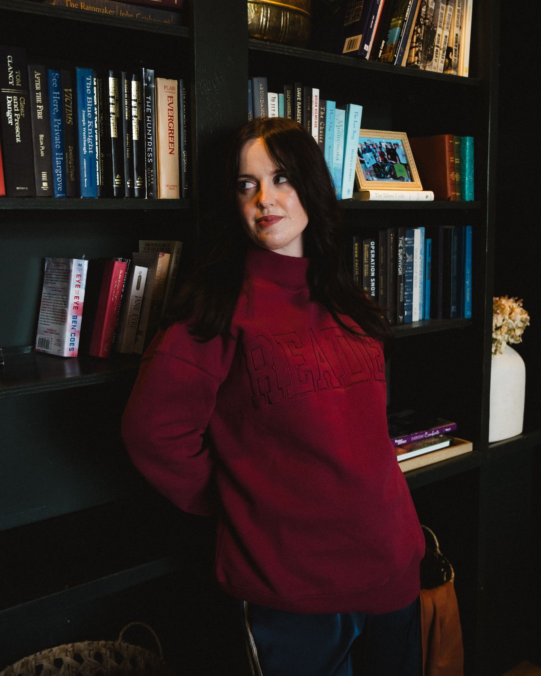 The Reader Mock Neck sweatshirt from Next Chapter is a beautiful berry, dark magenta color with an embroidered 'reader' design across the front. It's the perfect cozy bookish sweater for readers and book lovers.