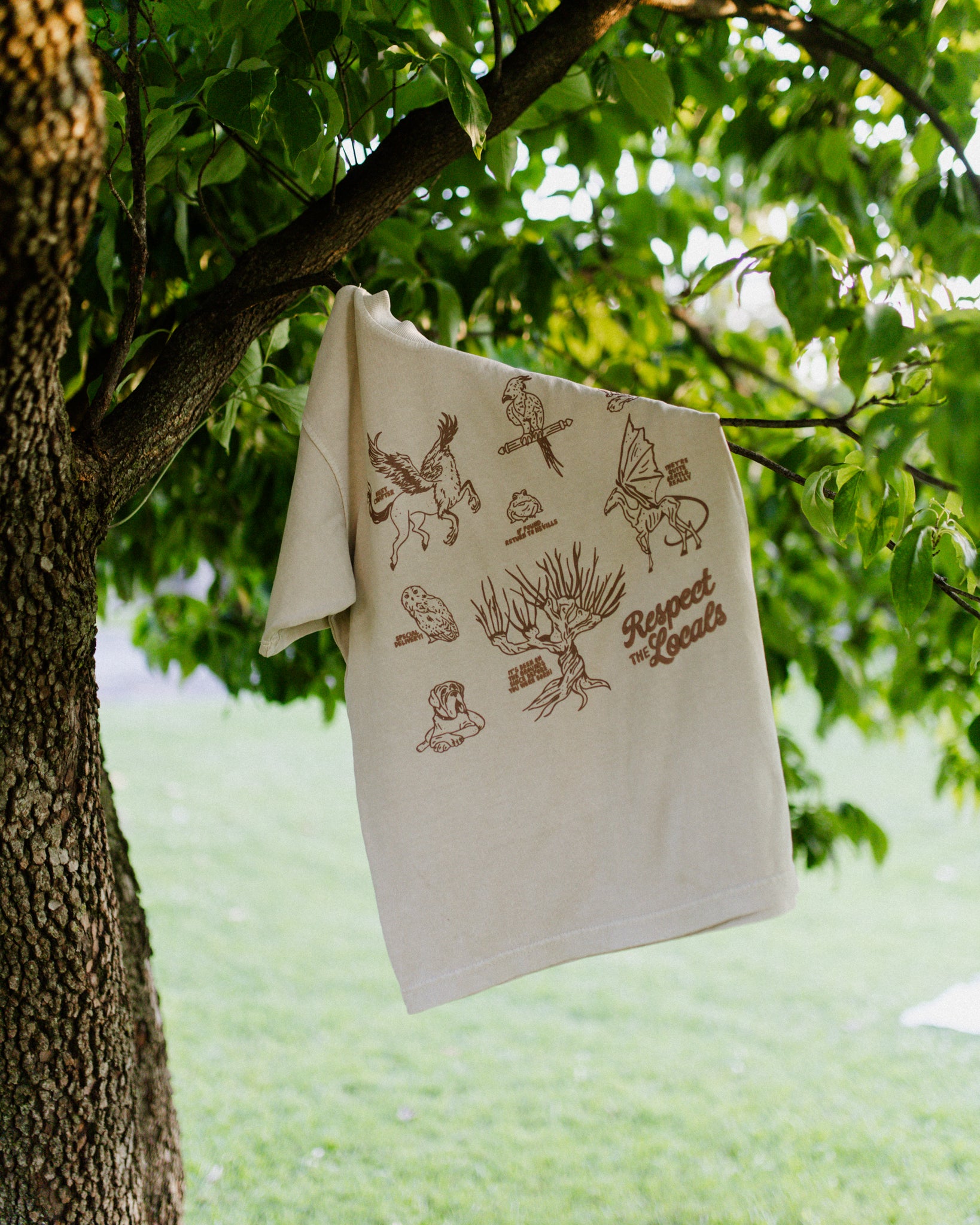Beige t-shirt with a brown design depicting creatures from Harry Potter hanging from a tree.