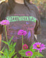 A woman wearing the Sweetwater Peak Tee from Next Chapter, inspired by the book Free Falling by Lyla Sage