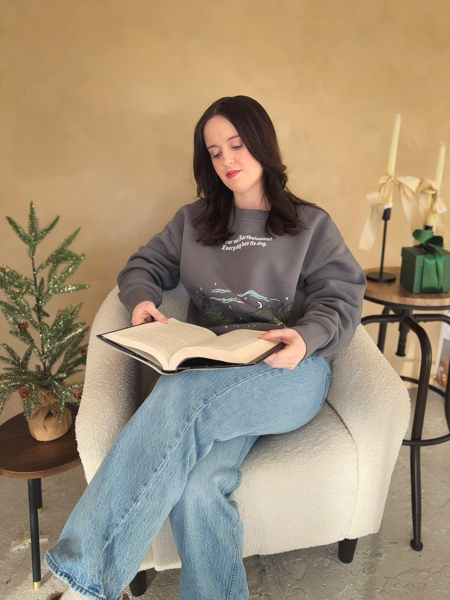 The Unlikely Trio Crewneck sweatshirt is dark gray with 'Fear not, Bartholomew! Every day has its dog' text and a colorful graphic design. Officially licensed Rachel Gillig merch. The Knight and the Moth merch. 
